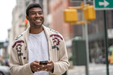 Young black man in city walking street texting on cellphone