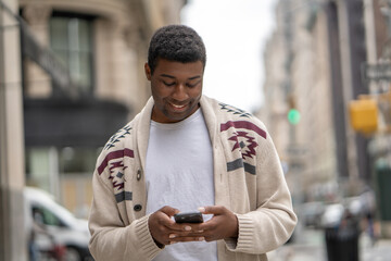 Young black man in city walking street texting on cellphone