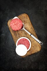 Patty Press with Burgers on Wooden Board on Black Background, Overhead View. Plastic Burger Press and Stuffer With Grill Tools. Beef and Pork Mince Patties.