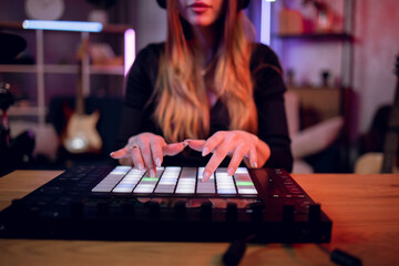 Selective focus of female musician mixing music on dj controller while recording song at studio. Young woman creating new track while sitting at table at dark room.