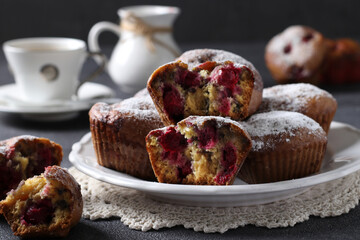 Muffins with cherries sprinkled with powdered sugar on a white plate on a dark background. Close-up.