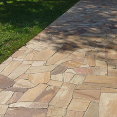 Garden landscaping with Pavement from Tiled Limestone. Backyard Garden Shaded Footpath from Tiled Stone Slabs. Flagstone Walkway in The Garden. Shady Pathway From Stone Tiles In The Park.