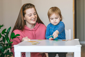 Fototapeta premium Young mother and one and a half year old girl collects puzzles. Psychomotor skills and the development of logical thinking 