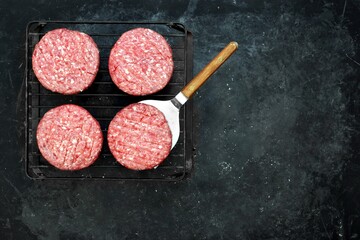 Grill Barbecue Grate with Raw Beef Hamburger Patties. Ground Beef Patties for Grilling and Roasting. Raw Minced Steak Burgers from Beef Meat on Black Background. Burger Cutlets On Paper And Grate.