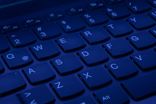 QWERTY Keys of a laptop computer keyboard illuminated with uv ultraviolet purple light