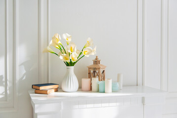 Soft home decor, white jug, vase with white and yellow beautiful flowers on a white wall background and on a wooden shelf. Interior. © Olena Svechkova
