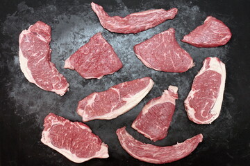 Various Raw Steaks. Sirloin Beef Steaks, Overhead View. Many Raw Striploin Steaks from Marbled Beef on Black Background. Group of Black Angus Beefsteaks. Raw Sirloin Cuts. Uncooked Prime Beef Steaks.