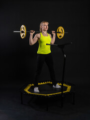 Fototapeta premium Girl on a fitness trampoline on a black background in a yellow t-shirt trampoline energy active activity caucasian movement, muscular club. Fly white motion, physical muscle instructor enjoy