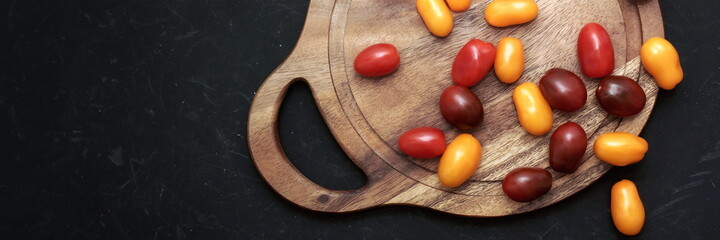 Plum Cherry On White Round Cutting Board. Assorted Plump Cherry Tomatoes On Wooden Cutting Board. Scattered Red, Yellow And Black Plum Cherry Tomato On Black Grunge Background.