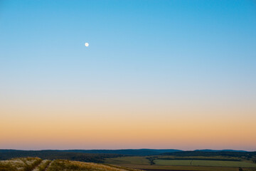 Sunset and moon over the field and forest.