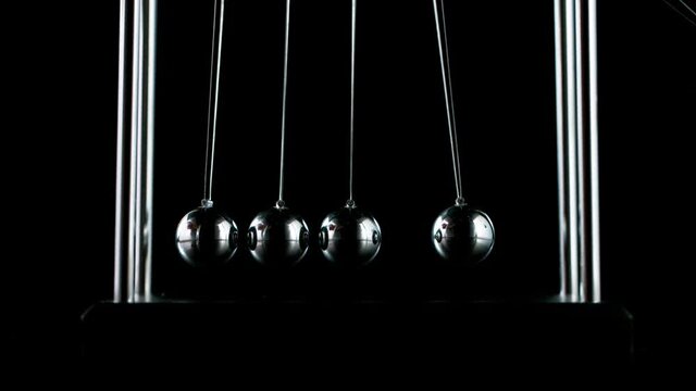Slow motion shot of swinging metal balls on black background. Newton's cradle.