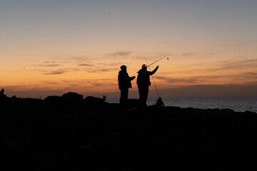 Fototapeta na wymiar Silhouettes of two fishermen getting ready at sunset to fishing