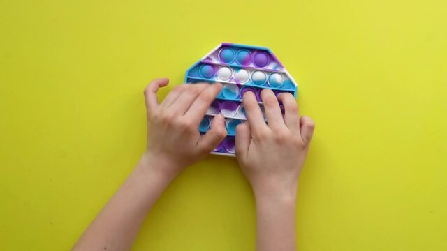 Popit antistress toy for children entertainment on a yellow background playing a child top view in colored fijit simple dimple popit game children, relief funny idget ubble, plastic kid. Top