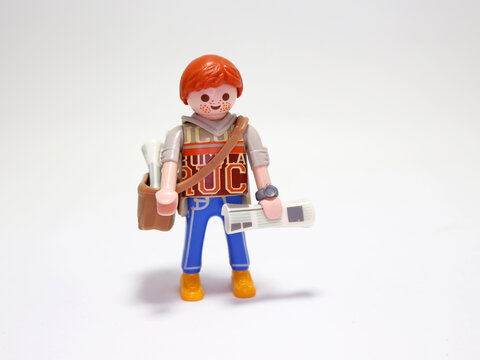 Playmobil doll. Newsboy. New's paper seller. Young boy. Paperboy. Newspaper. Redhead with freckles. Boy. Employee. Happy person. Isolated white. Toy.