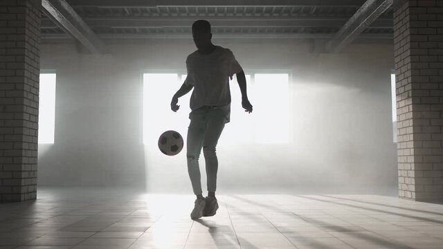 Black man football soccer player practicing tricks, kicks and moves with ball inside empty covered parking garage. African boy freestyle training in Urban city . Slow motion RAW graded footage