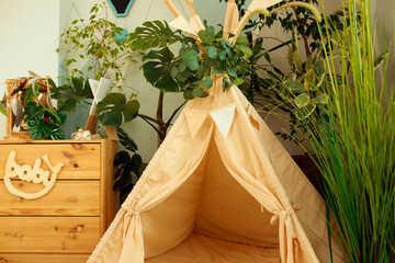 interior of a children's room or recreation area: a wigwam with soft pillows, a wooden nightstand made of environmentally friendly materials. plastic plants to decorate the space © skeronov