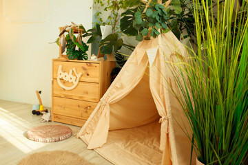 interior of a children's room or recreation area: a wigwam with soft pillows, a wooden nightstand made of environmentally friendly materials. plastic plants to decorate the space © skeronov