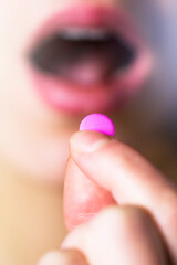 Young girl puts a pink vitamin pill in her mouth. Health and self-care.