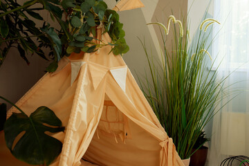 interior of a children's room or recreation area: a wigwam with soft pillows, a wooden nightstand made of environmentally friendly materials. plastic plants to decorate the space © skeronov