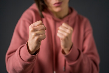 A girl in a pink hoodie is boxing on a dark gray background. The image of a brave young woman who successfully struggles with life's difficulties and develop her character and motivation.