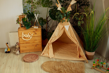 interior of a children's room or recreation area: a wigwam with soft pillows, a wooden nightstand made of environmentally friendly materials. plastic plants to decorate the space © skeronov