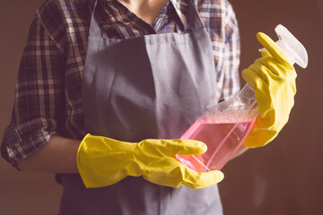 Young female hands in yellow rubber gloves hold a new detergent for cleaning the house and wiping...