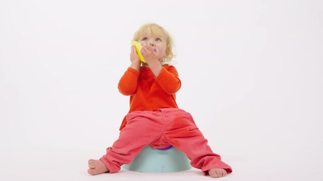 Adorable cheerful toddler girl sitting on potty talking on her smartphone enthusiastically isolated on white studio background. smart kid learns Internet technology. Getting baby accustomed to potty