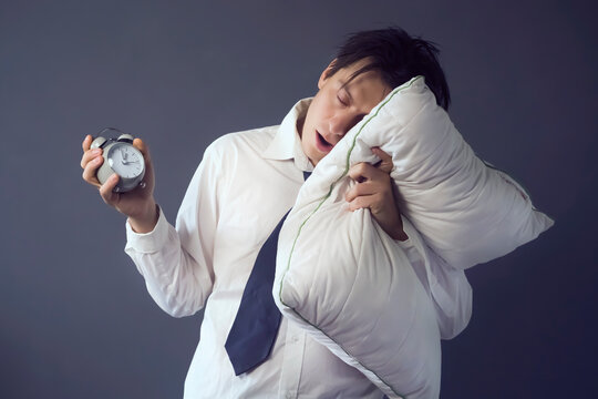 A Young Funny Man In A White Shirt And Tie With Disheveled Hair Slept Through The Deadline, Holding A Vintage Alarm Clock In His Hand. The Office Worker Is Overworked And Tired.