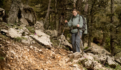 A young girl in hiking clothes walks with trekking poles along the trail in the mountains and forest in spring. A woman walks in the national park.