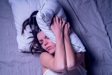 A young girl woke up in the morning in bed with a severe headache after the stress at work and nerves. The woman has insomnia and discomfort, feeling pain.