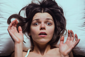 Young girl with a frightened expression wakes up from a nightmare in bed. Woman had a terrible...