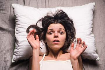 Young girl with a frightened expression wakes up from a nightmare in bed. Woman had a terrible...
