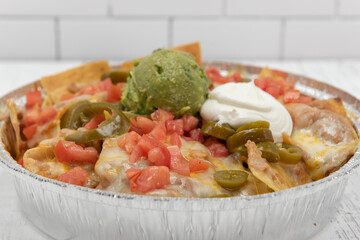 Large tin full of melted nachoes covered in melted cheese, jalapenos, sour cream, and guacomole