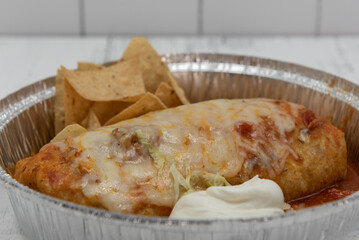 Wet burrito smothered in melted cheese and served with rice and sour cream in large tin