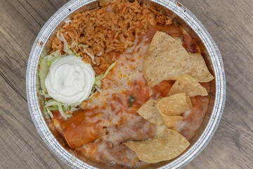 Overhead view of large tin holding an enchilada covered in melted cheese, served with refried beans, and rice