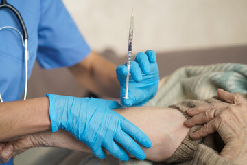 The nurse makes an injection with the vaccine to the patient at home. A young doctor in a blue suit...