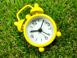 Alarm clock on grass background. Time concept. Yellow alarm clock with fresh green grass with copy space.