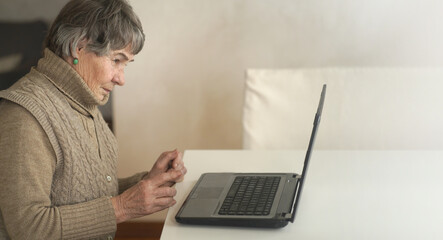        Old woman wearing casual clothes such as knitted sweater, spending free time at cozy home, sitting,  resting using pc, typing message and searching, reading news online.