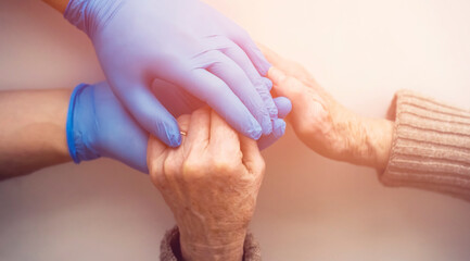 Fototapeta premium A doctor's hands in a blue gloves holds the hands of an elderly woman, a patient. Handshake, caring, trust and support. Medicine and healthcare.