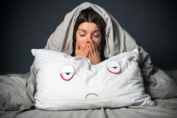 Girl hugs a pillow with tired red eyes and a sad expression on her face, hides under the covers....