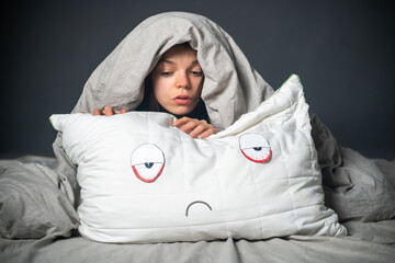 Girl hugs a pillow with tired red eyes and a sad expression on her face, hides under the covers....