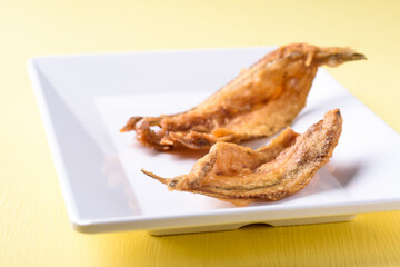 Fried dry fish on white dish with yellow background, Asian cuisine