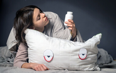 A young tired girl takes sleeping pills and hugs a pillow with red, puffy eyes from insomnia. The...