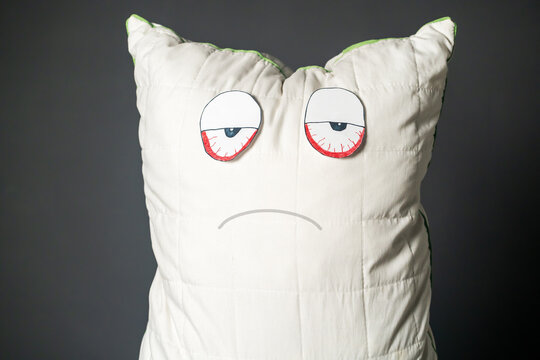 A pillow with added expressive face and red eyes as an image of a tired person who wants to rest, suffering from overwork, insomnia and depressive states.