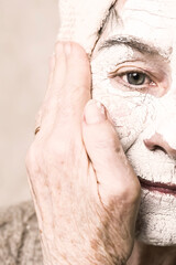 Elderly woman takes care of appearance, smiles in a white natural mask with vitamins for lifting, regenerating and rejuvenating the skin of the face. Pensioner makes beauty treatments in the bathroom.