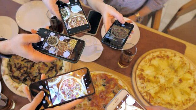 A young group of friends takes photos of food on their smartphone.