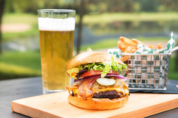 A bacon cheeseburger with French fries and a glass of beer.
