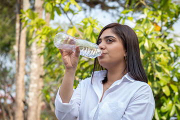 Joven Mujer en parque tomando descanso y bebiendo agua