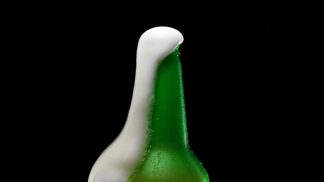 Beer foam escapes from bootle on black background