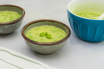 Creamy celery soup with green peas and fresh basil close up in bowls on light grey marble background